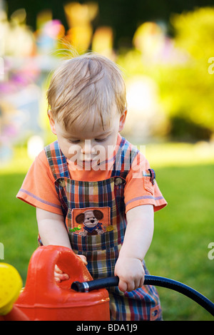 Portrait of a toddler playing with garden hose and watering can in the garden Stock Photo