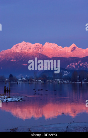 Sun setting on Golden Ears reflected in Pitt River, waterfowl fly low over the river, Port Coquitlam, British Columbia, Canada Stock Photo