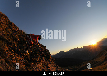 Mountain biker Rowan Sorrell rides a rocky ridge at sunset high above Sauze d'Oulx in the Italian Alps Stock Photo