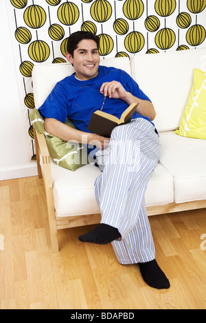 Portrait of a mid adult man sitting on a couch and holding a book Stock Photo