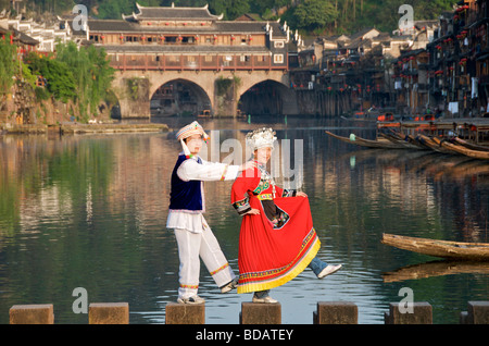 Couple in minority costume posing for photos with Hong Qiao Bridge in background Ancient Town of Fenghuang Hunan China Stock Photo