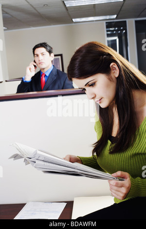 Businesswoman reading a newspaper with a businessman talking on a mobile phone in the background Stock Photo