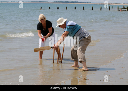 Man and woman playing cricket at the seaside retired couple enjoying healthy exercise on the beach Stock Photo