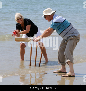 Man and woman playing cricket at the seaside retired couple enjoying healthy exercise on the beach Stock Photo