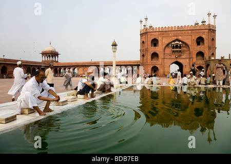 Muslim male worshipers ceremonially wash in water pool, with Eastern Gate of the Jama Masjid (Great Mosque) behind. Delhi. India Stock Photo