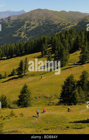 Three mountain bikers ride across an alpine meadow high in the mountains above Sauze D'oulx in the Italian Alps Stock Photo