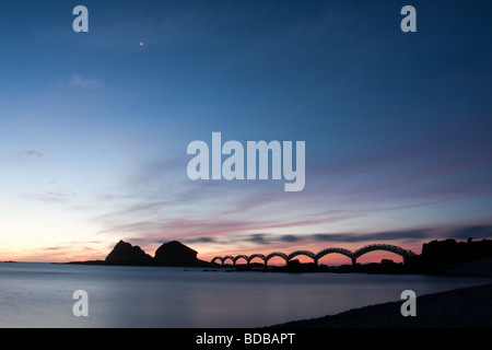 A small island off the coast and the iconic eight-arch footbridge silhouetted against twilight sky, at Sanxiantai in Taitung, Taiwan Stock Photo