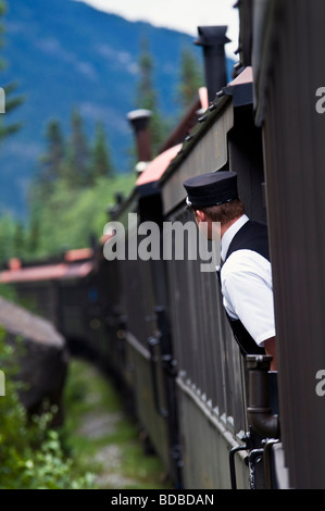 Skagway Alaska, The Brake Conductor on the White Pass and Yukon Route Railway leans out from between cars for a better view. Stock Photo