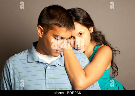 Male female couple posing together in studio in front of a neutral colored backdrop.  Woman is resting hands on shoulder of man. Stock Photo