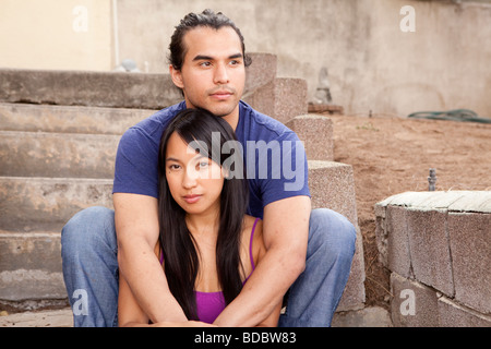 Male and female couple sitting on concrete steps, his arms are around her.  Looking at camera.  Woman is Filipino. Stock Photo