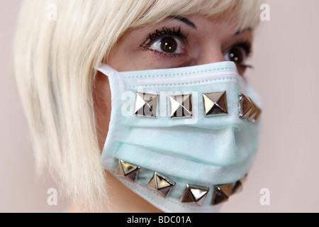 A scared girl  looks straight ahead. She wears a customized surgical face mask with studs. Stock Photo