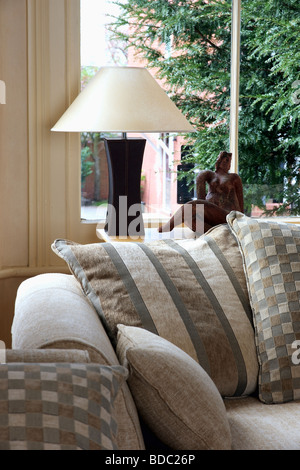 Patterned beige cushions on sofa in front of window with white and black lamp on window sill Stock Photo
