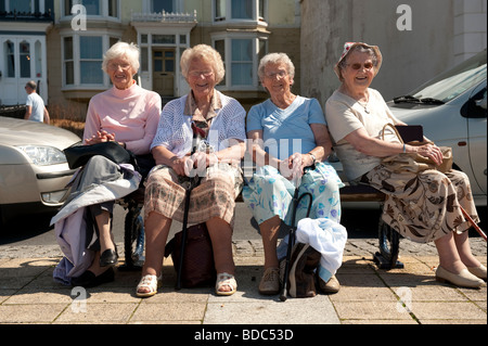 Four elderly women on a day trip to the seaside, sitting on a bench on summer afternoon Stock Photo