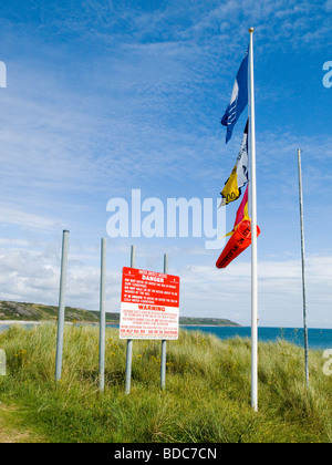 A warning notice and flags flying by the beach in Port Eynon, Gower Peninsula Swansea Wales UK Stock Photo