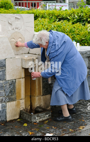 Elderly woman fills a plastic bottle with holy water from a tap, outside Our Lady of Knock Basilica, Ireland Stock Photo