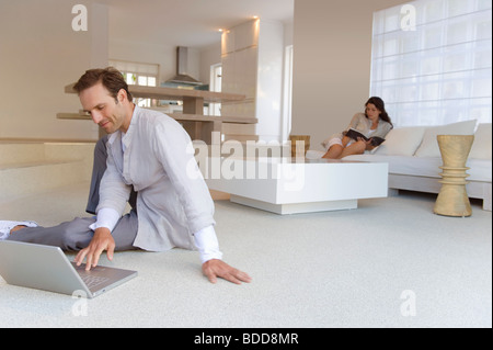 Man working on a laptop with a woman reading a book in the background Stock Photo