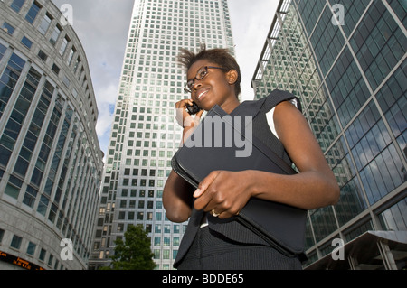 An attractive African business woman talking on her mobile phone at Canary Wharf with modern office buildings in the background. Stock Photo