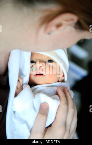 A five day old newborn child is lifted out of an incubator by his mum. Model released Stock Photo