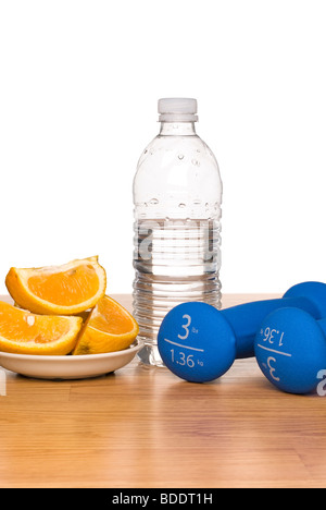 A conceptual image of healthy living including exercise equipment, a bottle of water and a sliced orange. Stock Photo