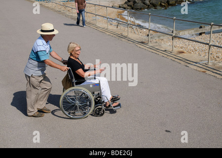 Man pushing woman in a wheelchair on the seafront at Bognor Regis West Sussex southern England UK Stock Photo