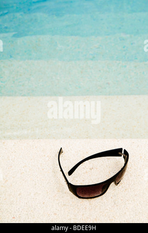 A pair of sunglasses on the edge of a swimming pool