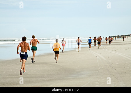 Runners running down the beach in a race by the ocean on the sand in ...