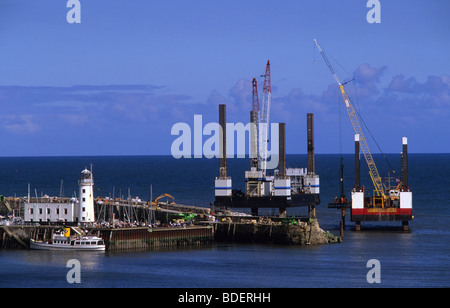 the pleasure ship coronea moored at Scarborough harbour by giant cranes on sea platforms constructing sea defences Yorkshire UK Stock Photo