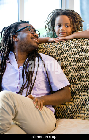 Jamaican father and young son with dreadlocks on sunroom on sofa Stock Photo