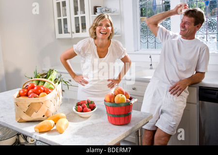 Mid adult couple laughing in kitchen with fresh fruits and vegetables Stock Photo