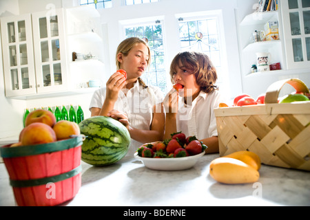 Boy and girl in kitchen eating fresh fruits Stock Photo