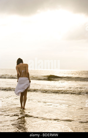 Rear view of young woman in white bikini and skirt walking in ocean at beach Stock Photo