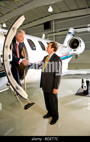 Middle-aged businessmen shaking hands at private jet plane Stock Photo