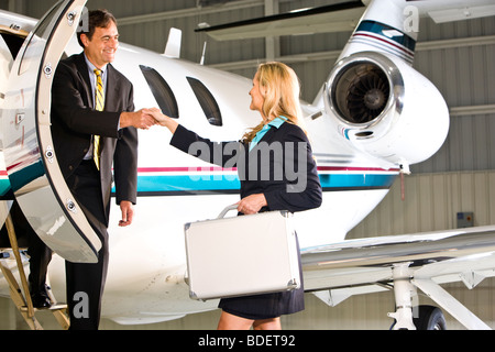 Businesspeople shaking hands outside small private jet Stock Photo