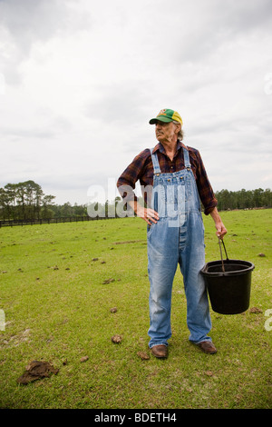 Farmhand in overalls carrying bucket in green pasture Stock Photo