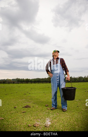Farmhand in overalls carrying bucket in green pasture Stock Photo
