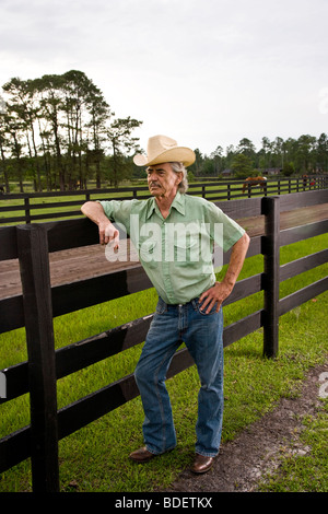 Senior man wearing cowboy hat on ranch leaning on fence Stock Photo