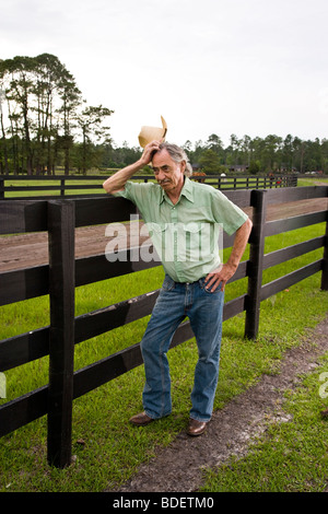 Senior man wearing cowboy hat on ranch leaning on fence Stock Photo