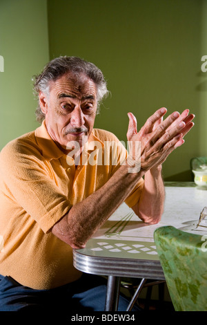 Senior man sitting at kitchen table gesturing with hands Stock Photo