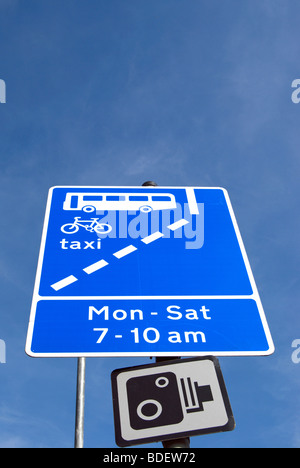 road traffic sign indicating a bus lane also used by taxis and cyclists and its hours of operation, with a cctv sign beneath Stock Photo