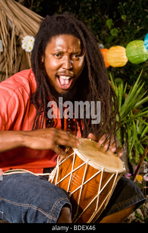 Young Jamaican man with dreadlocks playing bongo on tropical island Stock Photo