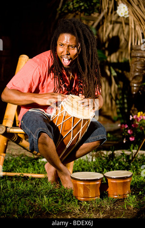 Young Jamaican man with dreadlocks playing bongos on tropical island Stock Photo