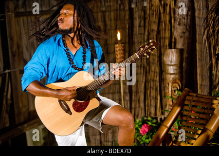 Young Jamaican man with dreadlocks playing guitar on tropical island Stock Photo