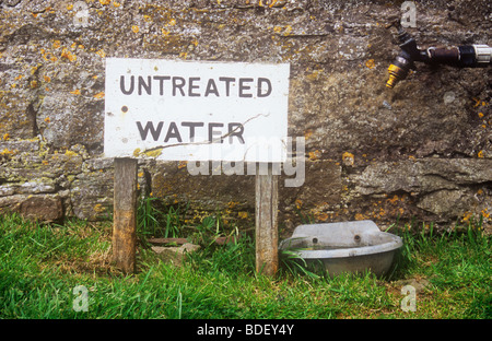 Sign in front of stone wall beside large water bowl and below outside tap stating Untreated water Stock Photo