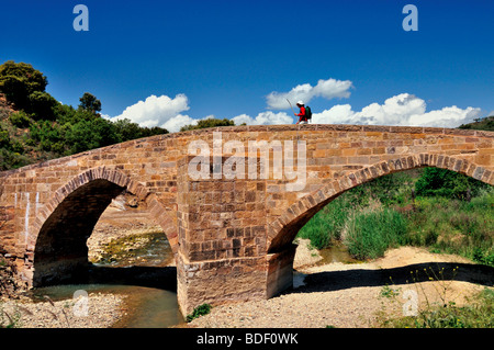 Spain, St. James Way: Pilgrim passing medieval bridge over river Salado between Estella and Cirauqui Stock Photo