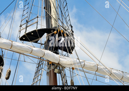 Sailing ship mast detail showing sail furled on yardarm, mast top, shrouds, lines, rigging and halyards Stock Photo