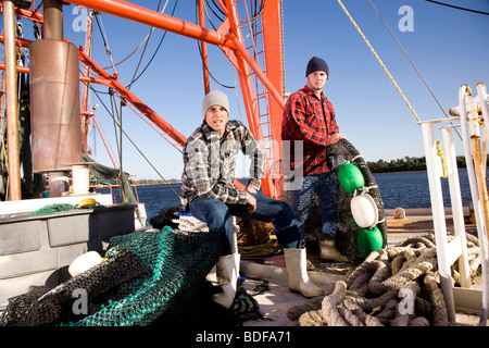 Young fishermen in plaid shirts on fishing boat with nets Stock Photo