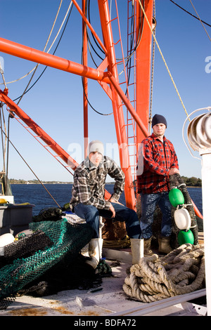 Young fishermen in plaid shirts on fishing boat with nets Stock Photo