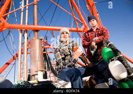 Young fishermen in plaid shirts on fishing boat with nets and wrench Stock Photo