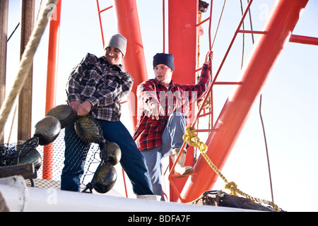 Young fishermen in plaid shirts pulling nets on fishing boat Stock Photo