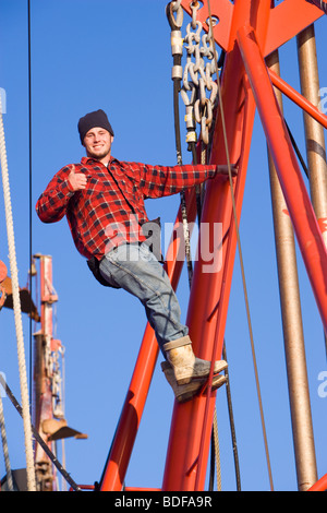 Young fisherman in plaid shirt climbing on fishing boat and giving thumbs up Stock Photo